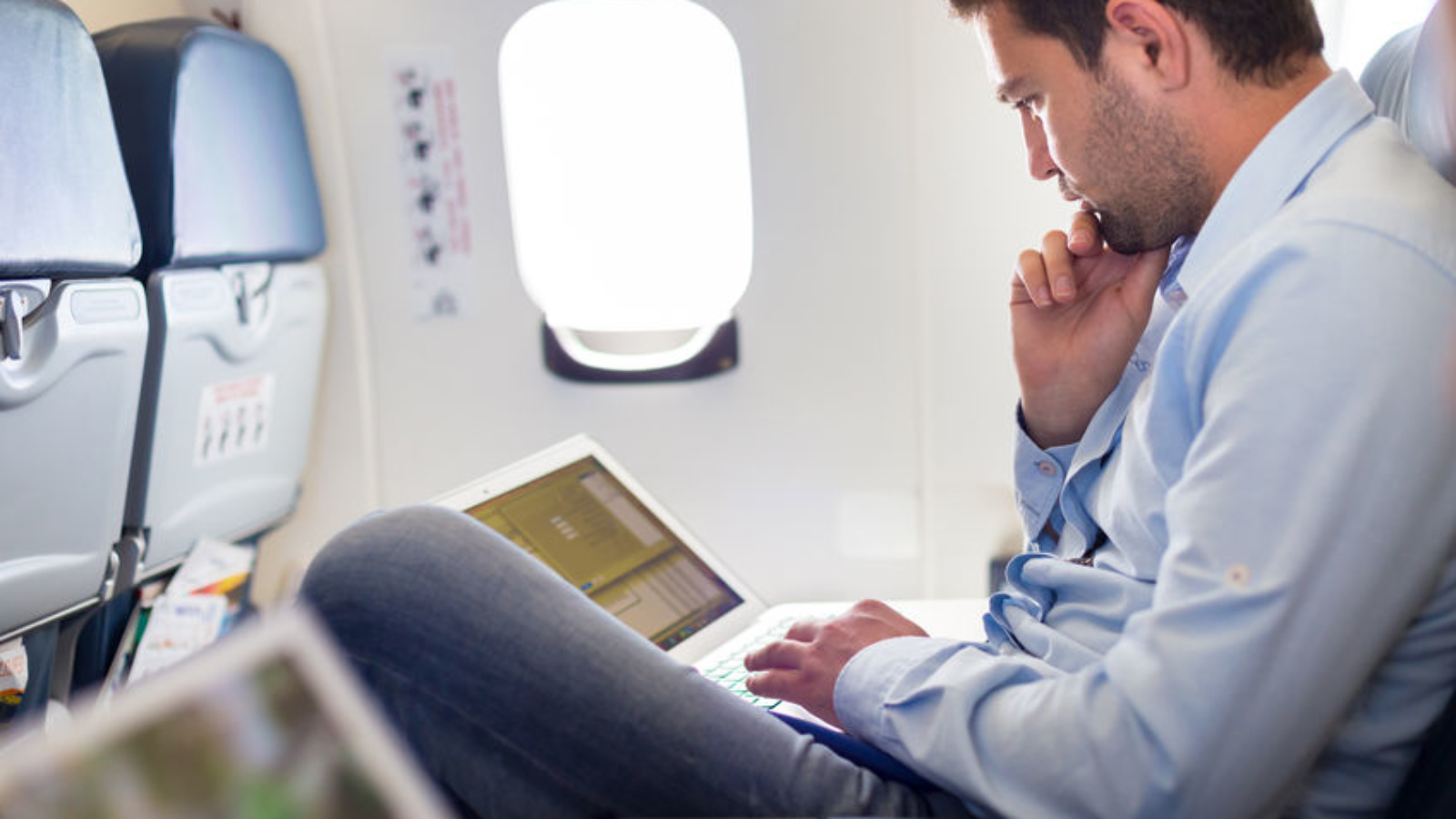 45104975 - casually dressed middle aged man working on laptop in aircraft cabin during his business travel. shallow depth of field photo with focus on businessman eye.